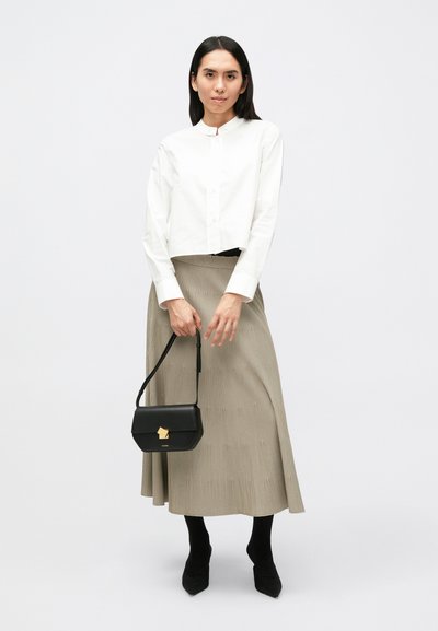 Λευκό cropped πουκάμισο με κουμπιά, μπεζ πλισέ φούστα, μαύρη τσάντα με χρυσό κούμπωμα και μαύρα παπούτσια με μυτερή μύτη. Λείο ύφασμα και δομημένος σχεδιασμός.