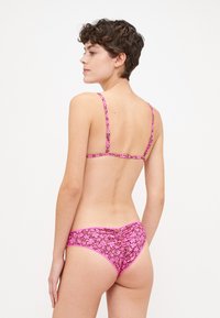 Rózsaszín virágmintás bikini vékony pántokkal és redős hátrésszel. Az anyag sima tapintású, kontrasztos virágmintával rendelkezik.