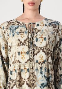 Ελαφρύ, πουκάμισο με σχέδιο σε κρέμ απόχρωση με μπλε, καφέ και πορτοκαλί μοτίβα. Διαθέτει λαιμόκοψη με κόμπο και κουμπιά μπροστά.