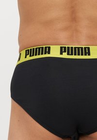 Fekete férfi alsónadrág sárga derékszíjjal, amelyen fekete "PUMA" logó található. Az anyag simának és rugalmasnak tűnik.