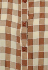 Camisa de botão em padrão xadrez castanho e bege, feita de um tecido com um acabamento texturizado. Apresenta botões castanhos ao longo da frente e uma bainha reta.