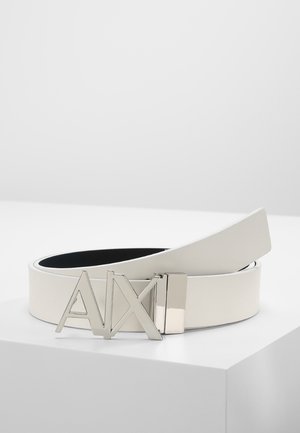 Weißer Ledergürtel mit silberner Metall-Schnalle, die große "A|X" Buchstaben zeigt, auf einer weißen Oberfläche aufgewickelt präsentiert.