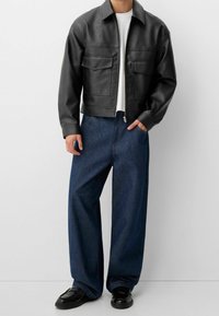 Zwarte leren jas met twee voorzakken, gecombineerd met loszittende donkerblauwe spijkerbroek en zwarte loafers. Witte T-shirt eronder.