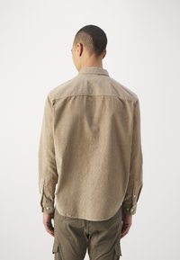 Camicia di corduroy marrone chiaro con colletto a bottoni, maniche lunghe e orlo dritto, caratterizzata da sottili righe verticali e polsini con bottone.