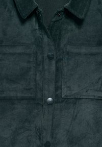 Dark green corduroy shirt with two chest pockets and black branded snap buttons down the front.