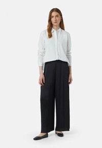 Witte button-down shirt, zwarte geplooide wijde broek en zwarte flats. Gladde stof met gestructureerde plooien; casual, professionele uitstraling.