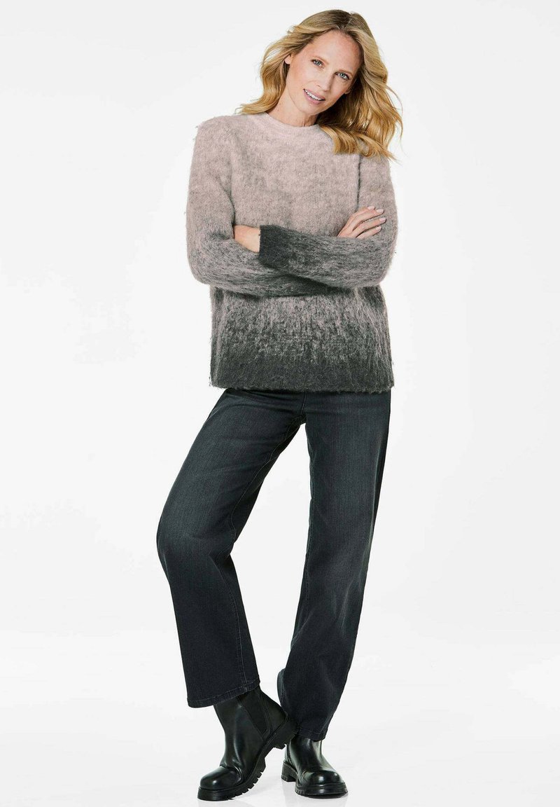 Übergroßer, gestrickter Pullover mit einem Ombre-Design, das von hellrosa zu dunkelgrau übergeht. Kombiniert mit dunkelblauen, geraden Jeans und schwarzen Stiefeln.