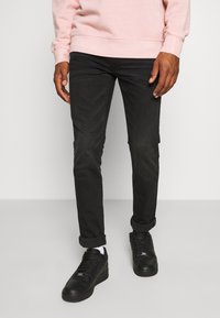 Jean noir slim avec un léger effet délavé, accompagné de baskets noires. Design simple avec des revers retroussés et un tissu texturé.