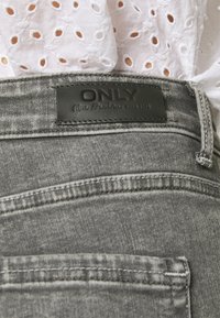 Jeans de mezclilla gris con una textura suave, parche de cuero con texto en relieve y detalles de costura minimalistas.
