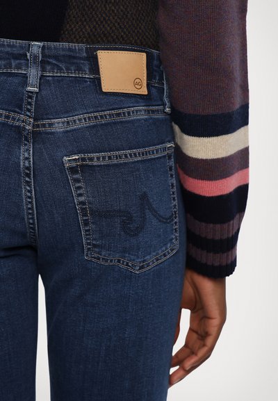Jeans de color azul oscuro con una etiqueta de cuero en la cinturilla, que presentan costuras curvas en el bolsillo trasero y una textura de denim suave.