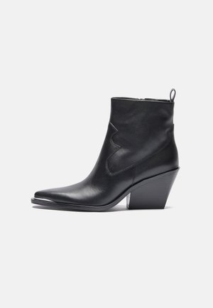 Bottine en cuir noir avec un bout pointu, un discret motif de couture western, et un talon empilé. Fermeture éclair sur le côté et une languette de traction.