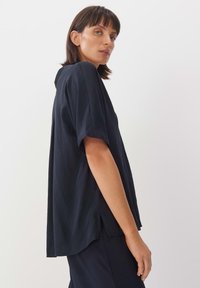 Marineblaues Kurzarmshirt mit einer lockeren Passform, aus leichtem Material gefertigt. Verfügt über seitliche Schlitze und eine subtile Textur.