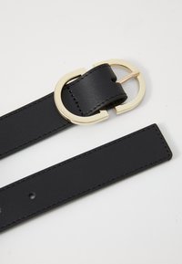 Mustaheräinen nahkavyö minimalistisella suunnittelulla, jossa on pyöreä kultasävyinen solki ja ompeluyksityiskohdat reunoilla.