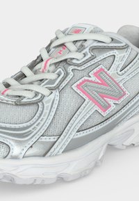 Γκρι και λευκό sneaker New Balance με ροζ λεπτομέρειες, πλεκτό επάνω μέρος και λευκά κορδόνια, που εμφανίζει το λογότυπο της μάρκας στο πλάι και στη γλώσσα.