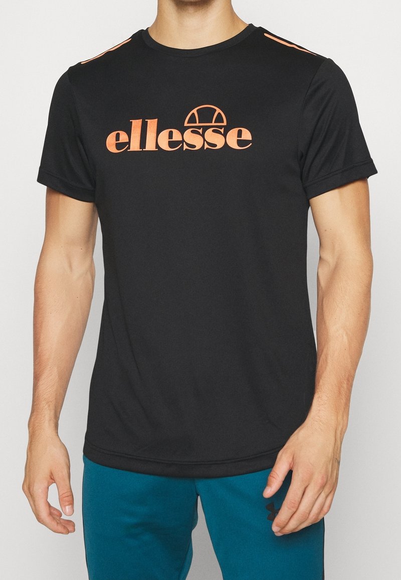 Man wearing a black short-sleeve t-shirt with orange "ellesse" logo and teal athletic pants with black logo on left thigh.