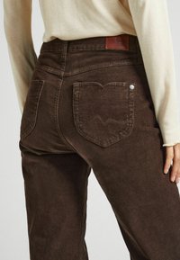 Bruine corduroy jeans met verticale textuur, voorzien van een kenmerkende hartvormige achterzak en een leren label op de tailleband.