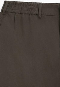 Pantaloni marrone scuro con tessuto testurizzato, dotati di una cintura elastica e pieghe anteriori sartoriali. Nessuna ferramenta o motivo visibile.