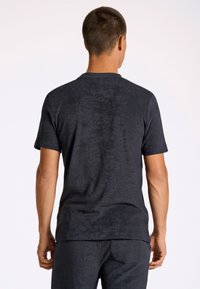 Czarny t-shirt z krótkim rękawem, wykonany z miękkiej, teksturowanej tkaniny. Posiada okrągły dekolt i luźny krój, noszony z dopasowanymi spodniami.