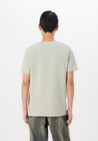 Ανοιχτό γκρι κοντομάνικο πουκάμισο με υφή, σχέδιο crew neck και χαλαρή εφαρμογή, συνδυασμένο με ξεθωριασμένα τζιν παντελόνια.