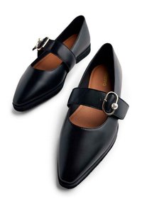 Ballerine in pelle nera con punta appuntita e una fascia larga con una fibbia in metallo. La fodera interna è marrone, creando un contrasto.