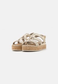 Flettede metalliske plattform sandaler i beige med korksåle. Har kryssede remmer og en justerbar ankelrem for bedre passform.