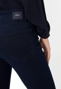 Brax donkerblauwe jeans, met een slim fit ontwerp, zachte denimtextuur en een enkele achterzak met zichtbare stiksels en merklabel.