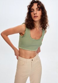 Vaaleanvihreä ribbed crop-top, jossa on röyhelöreunat ja leveä avara kaula-aukko. Yhdistetty korkeavyötäröisten beigejen farkkujen kanssa.