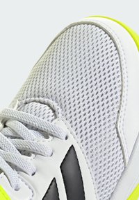 Sneaker bianca a rete con accenti grigi e suola gialla neon. Presenta un design con lacci testurizzati e punta rinforzata per una maggiore durata.