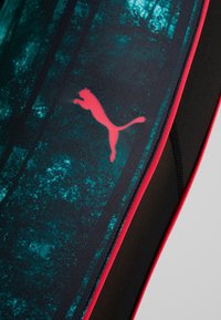Ingrandimento di leggings sportivi neri e teal con logo Puma rosso e rifiniture rosse sul pannello laterale.