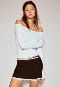Witte off-shoulder top met lange mouwen, gecombineerd met een zwarte rok met geribde zoom en voorzak. Gladde stof met een casual pasvorm.