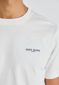 Hvit bomull t-skjorte med rund hals og en liten svart "PEPE JEANS LONDON"-logo på venstre side av brystet.