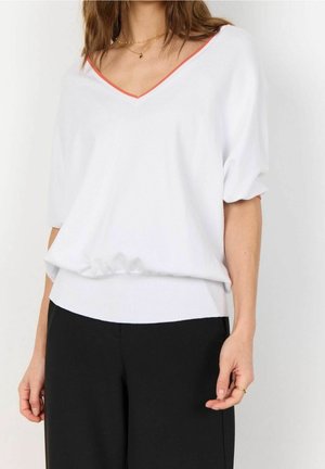 Pull-over blanc à col en V avec de courtes manches ballons, bordure contrastante orange au niveau du col, ourlet côtelé, associé à un pantalon noir. Tissu en tricot doux.