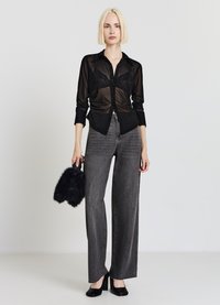 Camicia nera trasparente con bottoni sopra un bralette in pizzo nero, abbinata a jeans a gamba larga in denim grigio a vita alta e tacchi neri, mentre tiene una borsa di pelliccia.