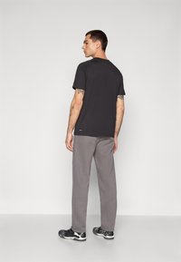 Mørkegrå t-shirt med korte ærmer, rund halsudskæring og diskret logo ved kanten, sat sammen med lysegrå joggingbukser og sorte sneakers.