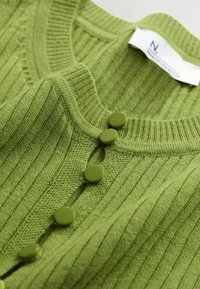 Zelený rebrovaný pletený cardigan s okrúhlym výstrihom a šiestimi zladenými gombíkmi. Mäkká textúra s uvoľneným strihom. Nálepka viditeľná na golieri.
