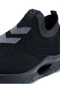 Schwarze Stricksneaker mit grauen Akzenten, die eine strukturierte Oberfläche, ein niedriges Design, einen elastischen Kragen und eine Gummisohle mit Rillen aufweisen.