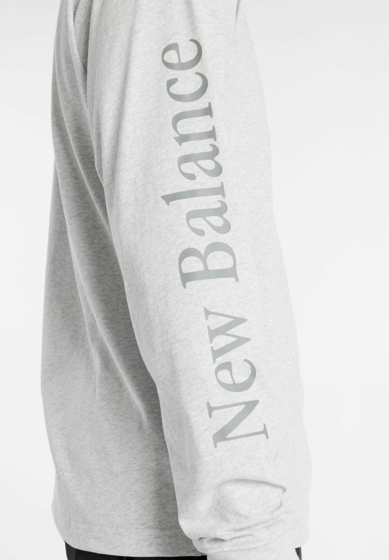 Long-sleeve gray shirt featuring "New Balance" printed vertically in light gray along the left sleeve; cotton blend fabric.