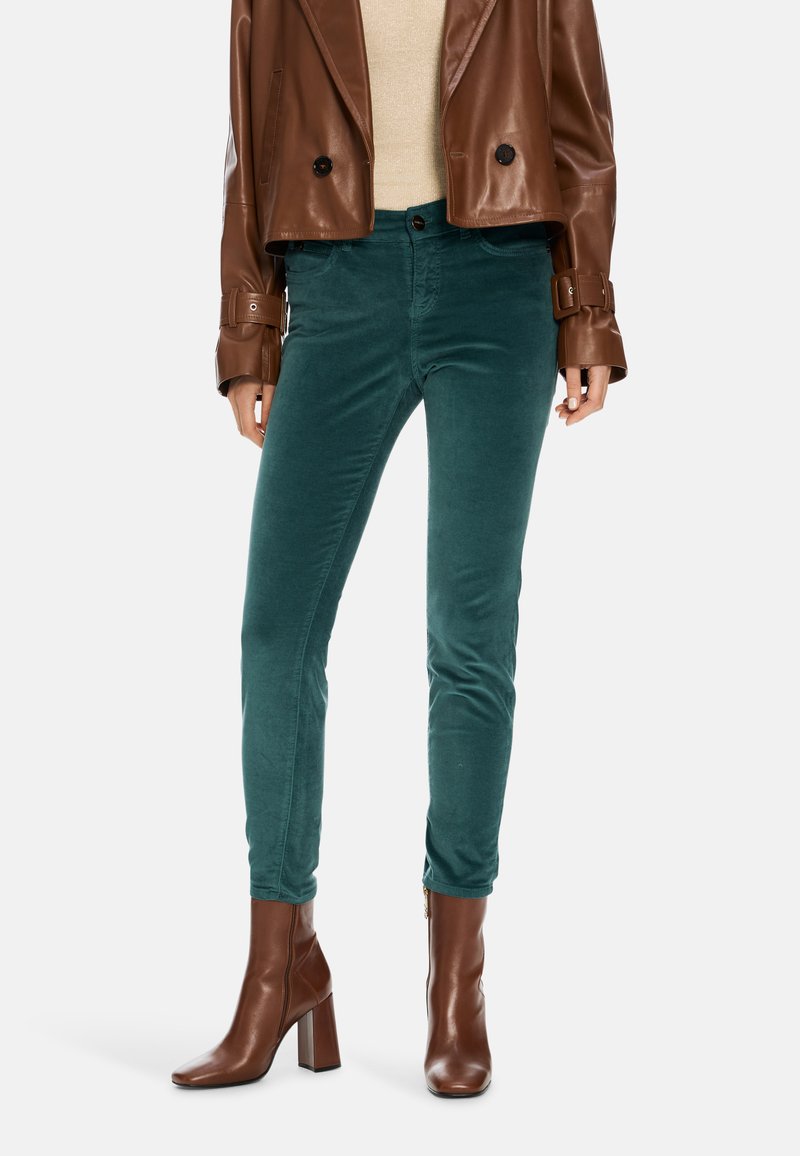 Teal velvety skinny pants with front pockets, paired with a brown leather cropped jacket and brown heeled ankle boots.