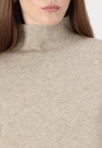 Beige ribbestrikket genser med høy krage. Myk tekstur, tettsittende design og minimalistisk stil uten mønstre eller detaljer.