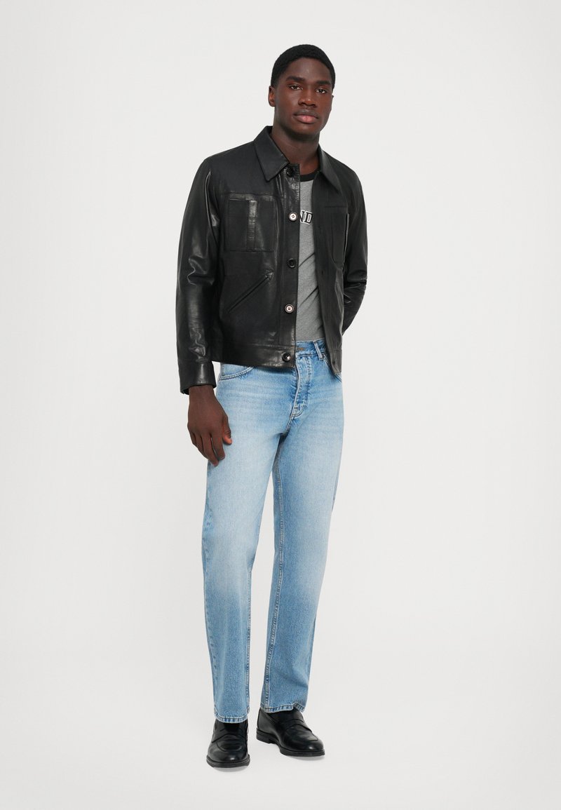 Sort læderjakke med forlommer, grå t-shirt, lyseblå jeans og sorte sko. Glat tekstur og klassisk design.