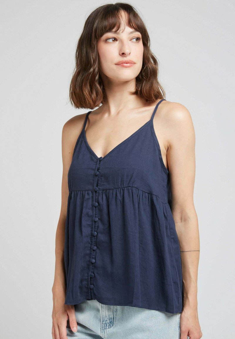 Blouse sans manches bleu marine avec un décolleté en V, des boutons sur le devant et une taille froncée. Fabriquée en tissu léger avec une texture douce.