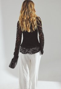 Black lace long-sleeve top with scalloped hem, paired with loose white linen pants. The top features intricate floral patterns and sheer sleeves.