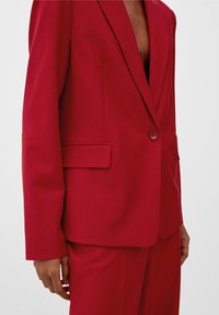 Veste de costume rouge avec une coupe ajustée, fermeture à un bouton, col à revers, poche latérale et tissu à texture lisse.