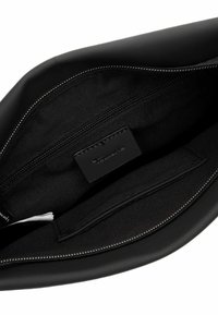 Svart läderväska inuti med dragkedjefack, platt fack och varumärkesetikett. Slät yta med minimalistisk design och silverfärgad dragkedjedetalj.