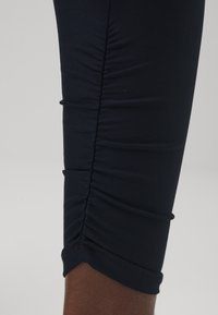 Marineblå leggings med mansjett har samlet tekstur, glatt syntetisk materiale, med en tettsittende design og elegant finish.