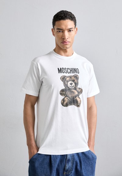 Tricou alb din bumbac, având un grafic mare cu un ursuleț de pluș și cuvântul "MOSCHINO" tipărit cu negru deasupra designului.