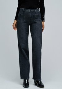 Vaqueros negros de cintura alta con un diseño de pierna recta. Presenta dos bolsillos frontales y una tela de mezclilla texturizada con costuras visibles.