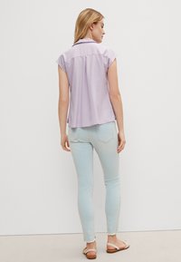 Light purple short-sleeve blouse, relaxed fit, with a rear pleat and collar, paired with light blue skinny jeans and tan sandals.