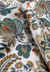 Tejido con fondo blanco que presenta patrones florales y de hojas en tonos azul verdoso, naranja y beige, con pequeños detalles en color óxido de calaveras y tibias.