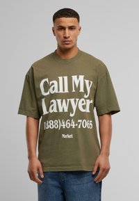 Oliven grøn bomulds t-shirt med oversized pasform. Fronten har stor hvid tekst med teksten "Ring til min advokat" og et telefonnummer.